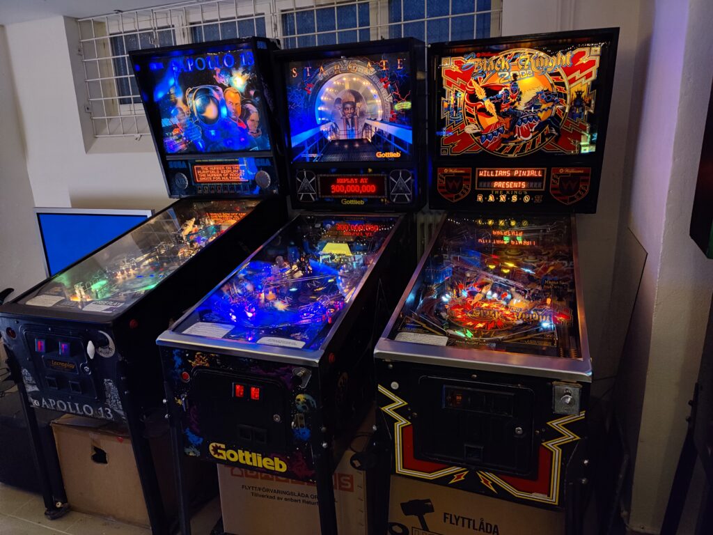 Tre upplysta flipperspel på rad i arkadhallen.