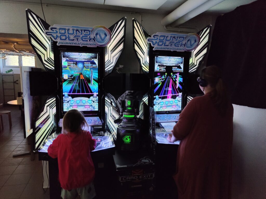 Två Sound Voltex-maskiner bredvid varandra med besökare som spelar.